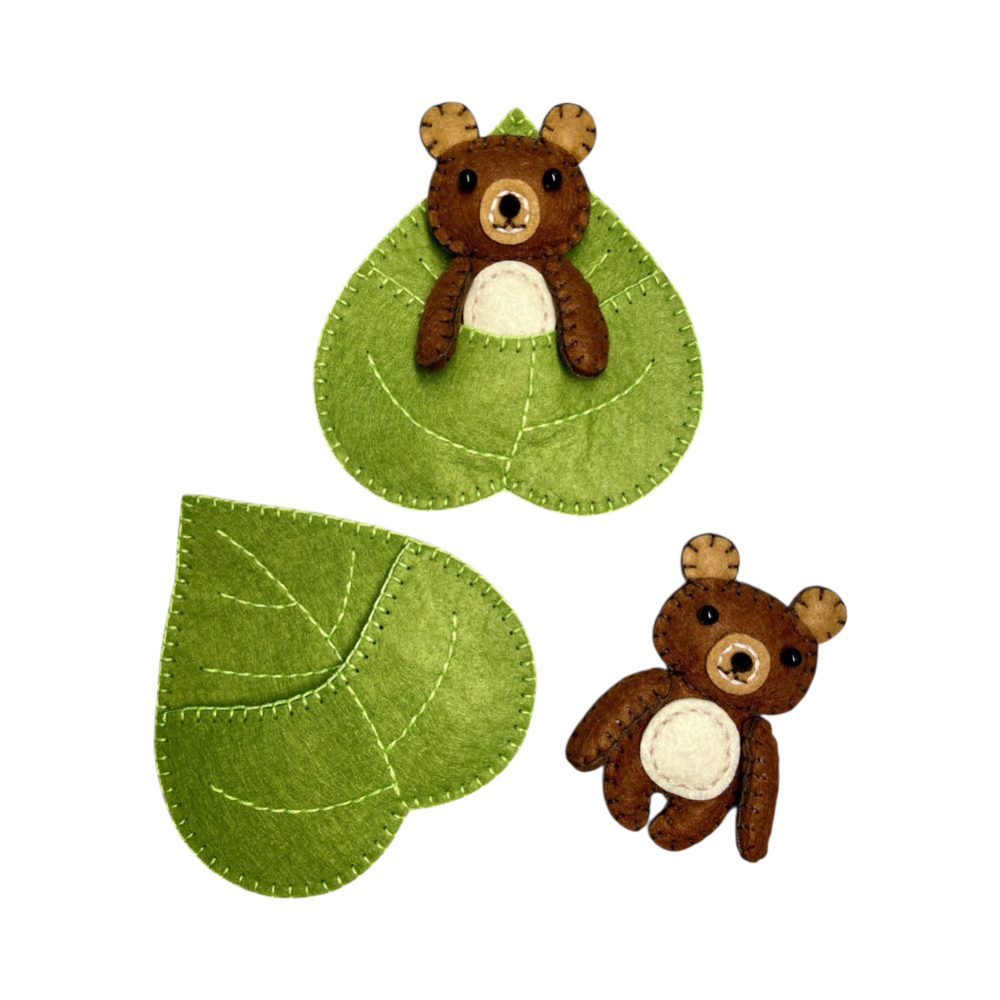 Two small brown teddy bears and green leaf-shaped felt pieces on a white background