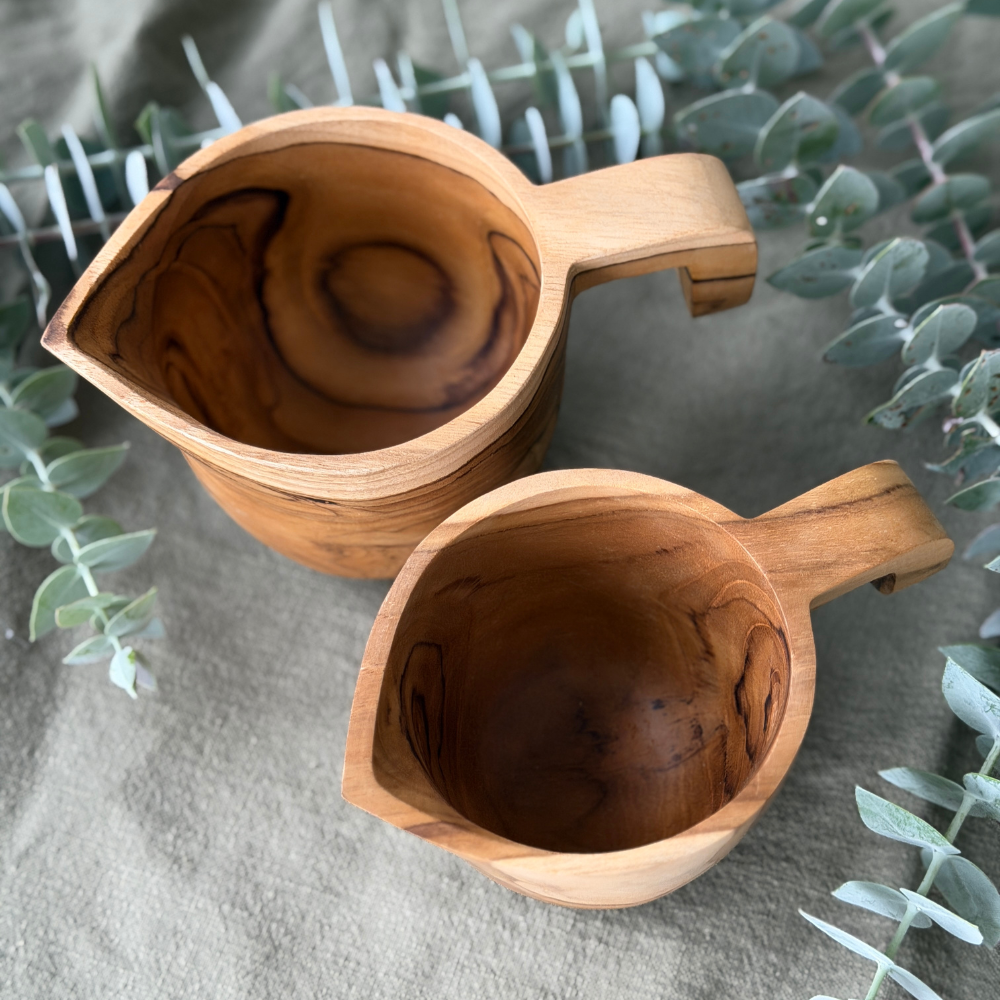 Two wooden jugs on a textured surface with greenery in the background