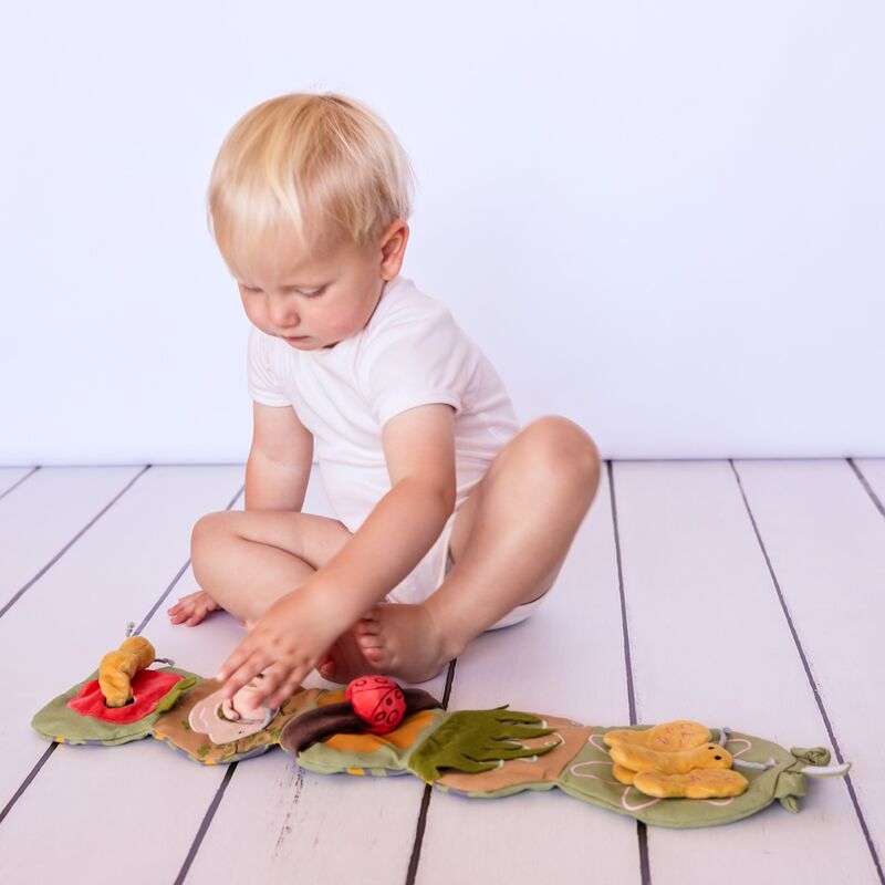 Child playing with a colourful caterpillar fabric book on a wooden floor