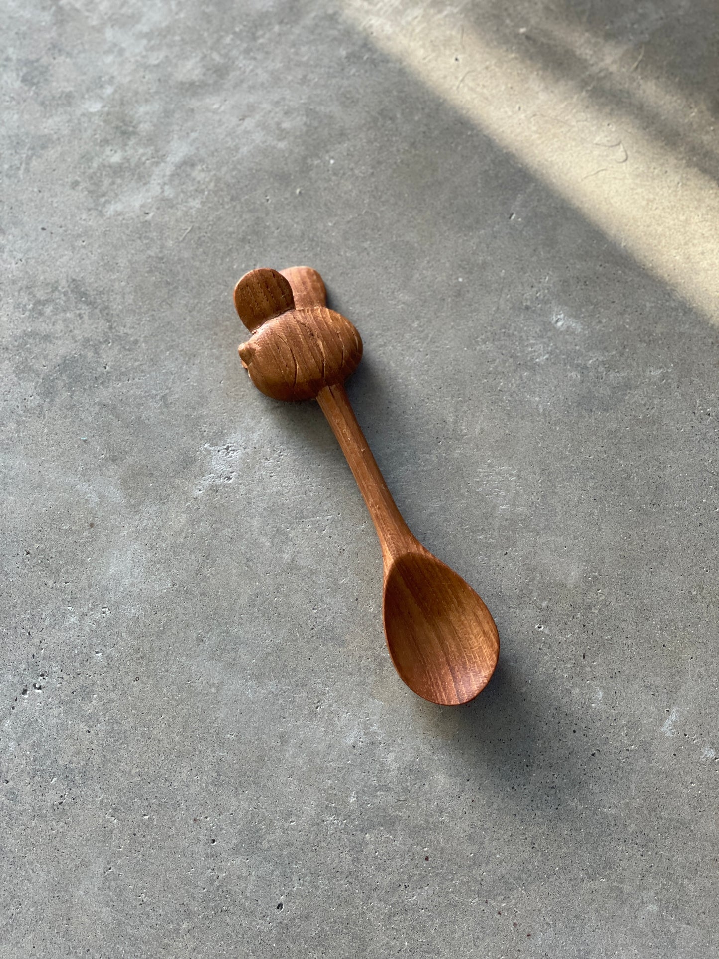 A hand-carved wooden spoon with a bee detail on the handle, placed on a grey surface.